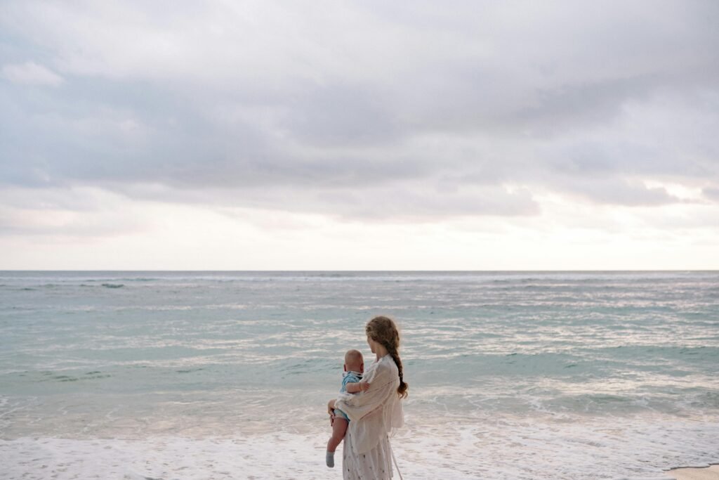 pexels-photo-4668987-4668987 A serene beach scene featuring a mother holding her baby by the ocean during summer.