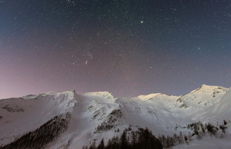 A breathtaking view of snow-capped mountains under a starry night sky, capturing the beauty of winter outdoors.